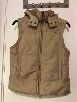 Grön dunväst med huva  - Säljer en grön dunväst från H&M i storlek XS. Västen har en avtagbar huva med mjukt fleecefoder, dragkedja framtill och två fickor på sidorna. Perfekt för lager på lager och enkel att matcha med olika outfits. Använd fåtal gånger. Pris kan alltid diskuteras!🤗