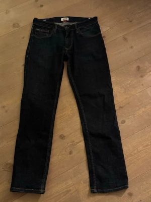Hilfiger Denim mörkblå jeans straight - Säljer ett par mörkblå Hilfiger Denim jeans i modellen Original Straight Fit. Klassisk femficksdesign, snygga kontrastsömmar och diskret Hilfiger-detalj vid fickan. Jeansen är raka i benen och har en tidlös look som funkar till allt. Storlek 32/32!