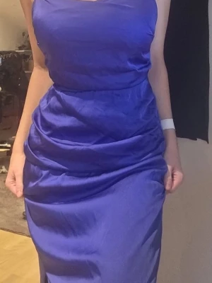 Blå långklänning från Bubbleroom - Säljer en elegant blå långklänning från Bubbleroom. Klänningen har en figurnära passform med draperade detaljer och är tillverkad i ett glansigt material som ger en lyxig känsla. Perfekt för dig som vill sticka ut med en stilren look.