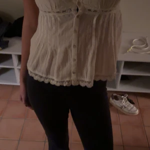 Vit spetsdetaljerad linnetopp från Zara - Supersöt vit linnetopp från Zara med tunna axelband, knappar framtill och vackra spetsdetaljer längs urringning och nederkant. Toppen har en luftig passform och är tillverkad i ett lätt material som känns fräscht och somrigt.