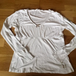 Vit ribbad långärmad topp Odd Molly - Supersöt vit långärmad topp från Odd Molly med ribbad struktur, v-ringning och liten rosett framtill. Toppen har diskreta volangdetaljer vid halsringningen. Storlek 4 (L). Skriv vid frågor💞
