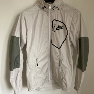 Nike jacka beige storlek S  - Nike jacka beige storlek S  Köpt på Intersport för många år sedan  Använd en del Liten fläck på insidan av jackan  Krage med luva inuti  Bröstvidd 54 cm x 2 = 108 cm Längd fram 70 cm Längd bak 74 cm