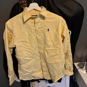 Gul skjorta från Polo Ralph Lauren M - Klassisk gul skjorta från Polo Ralph Lauren i bomull med broderad logga på bröstet. Skjortan har lång ärm, knappar framtill och en snygg krage. Perfekt för dig som gillar stilrena och tidlösa plagg.