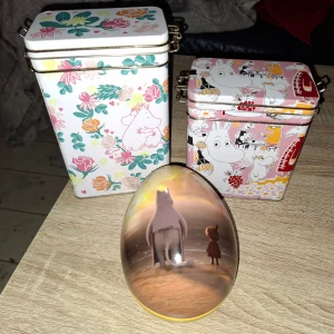 Mumin  - Bilderna visar fina Mumin-burkar och ett Mumin-påskägg, perfekta för samlare eller som dekoration. Burkarna har färgglada motiv med Mumin och vänner, och ser ut att vara i mycket gott skick utan synligt slitage. Perfekt för förvaring eller som present.