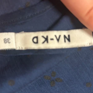 Blå blus med volangärm från NA-KD - Säljer en blå blus från NA-KD i storlek 38. Blusen har korta volangärmar, diskret blommönster och en liten knappdetalj bak. Tunt, lätt material som ger en luftig känsla. Perfekt för dig som gillar feminina detaljer och stilren look. Väldigt genomskinlig men sitter fint med ett linne under eller som den är.