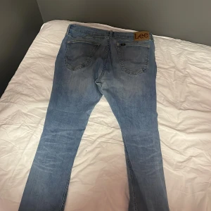 Ljusblå jeans från Lee - Säljer ett par ljusblå jeans från Lee med klassisk femficksdesign och Lee-lapp bak i midjan. Jeansen har raka ben och normal passform, tillverkade i mjukt denimtyg som ger en avslappnad vibe.