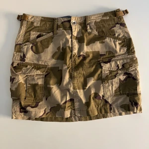 Camouflage lågmidjad kortkjol från G-Star RAW - Snygg kortkjol med låg midja från G-Star RAW i camouflage-mönster med flera praktiska fickor. Kjolen är tillverkad i bomull. Midjan är strl 25.