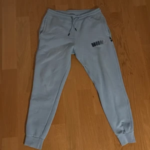 Ljusblå mjukisbyxor från Hoodrich M - Snygga ljusblå mjukisbyxor från Hoodrich med broderad logga på ena benet. Byxorna har snörning i midjan, muddar vid bensluten och är gjorda i mjukt bomullsmaterial. Perfekta för chill eller streetwear-stil.