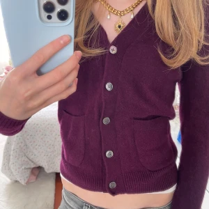 Mörklila kofta från Zara - Säljer superfin vinröd med en nyans av lila kofta från Zara med v-ringning och knappar framtill. Koftan har två fickor och är i mjukt stickat material, perfekt att slänga över en topp. Långärmad och sitter snyggt med normal passform. Är dock lite tajt i ärmarna.