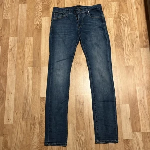 Blå jeans från Jack & Jones, 31/34 - Snygga blå jeans från Jack & Jones i klassisk straight fit. Jeansen har fem fickor, normal midja och subtila slitningar för en avslappnad look. Tillverkade i bomullsmix för skön känsla och bra passform. Perfekta till sneakers!