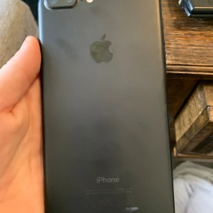 iPhone 7 Plus - iPhone 7 Plus i svart färg. Mobilen har dubbla kameror och klassisk Apple-design. Skärmen är kraftigt sprucken och behöver bytas ut, men baksidan ser relativt bra ut med mindre slitage. Perfekt för dig som vill reparera eller använda reservdelar.
