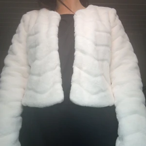 Vit pälsjacka med vågig struktur - Säljer en supermjuk och fluffig vit pälsjacka med vågig struktur. Jackan är kortare i modellen och har långa ärmar. Perfekt för dig som vill sticka ut med en stilren och trendig look. Jackan har två hyskor framtill för lättare stängning. 