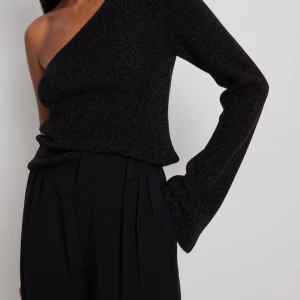 Svart glittrig stickad oneshoulder topp NA-KD - Säljer en svart glittrig oneshoulder topp från NA-KD i storlek XS. Toppen har en lång ärm och är ribstickad  perfekt nu till hösten! Köpt för 499kr & använd ett fåtål gånger! 