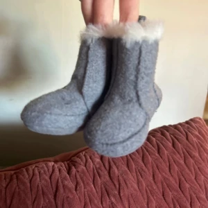 Gråa babyboots med fuskpäls - Supergulliga gråa babyboots med mjuk fuskpäls runt skaftet. Perfekta för att hålla små fötter varma under kyliga dagar. Tillverkade i mjukt syntetmaterial som känns skönt mot huden.