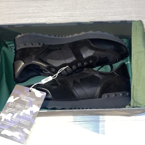 Valentino Garavani Rockrunner sneakers - Snygga svarta Valentino Garavani Rockrunner sneakers med coola kamouflagedetaljer och nitar på sulan. Skorna är tillverkade i en mix av skinn och mocka, har snörning och en chunky sula som ger en modern vibe. Perfekta för dig som vill sticka ut med stil. Helt oanvända!!