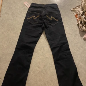 Mörkblå jeans med gult bakficksmönster - Snygga mörkblå jeans med klassiskt femficksdesign och coolt gult zigzag-mönster på bakfickorna. Jeansen har raka ben och normal passform, perfekta till sneakers eller boots. Materialet är robust denim som håller formen hela dagen.