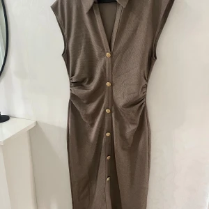 Klänning från zara - Snygg brun klänning med krage och guldfärgade knappar längs hela framsidan. Aldrig använd. 