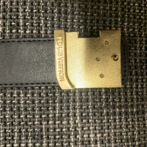 Louis Vuitton Damier skärp svart/guld - Snyggt Louis Vuitton bälte i svart skinn med klassiskt damier-rutmönster. Bältet har en ikonisk LV-spänne i guldmetall och exklusiva detaljer. Perfekt accessoar för att lyfta din outfit med lyxig känsla och stil.