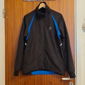 Svart och blå vindjacka Björn Dæhlie M - Säljer en svart och blå vindjacka från Björn Daehlie i storlek M. Jackan har dragkedja framtill, höga muddar vid ärmslut och två fickor med dragkedja. Snygga blå detaljer längs sidorna och ryggen. Perfekt för utomhusaktiviteter och träning. Kam gå ned i pris, kan mötas i skåne