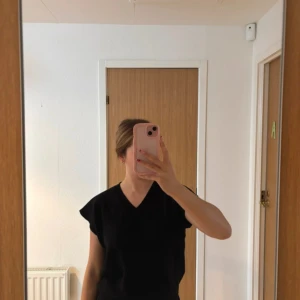 Svart topp med v-ringning från Amalia - Svart topp från Amalia med v-ringad hals och korta, voluminösa ärmar. Toppens material är ribbat och ger en snygg struktur. Perfekt för dig som gillar en enkel men stilren look.