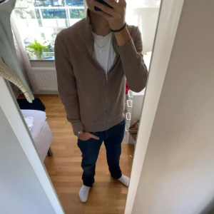 Beige stickad kofta med dragkedja - Säljer en stilren beige kofta. Den är ribbstickad, har lång ärm och hel dragkedja framtill. Enkel och clean design som passar till mycket. Perfekt för hösten och våren! Är i väldigt bra skick, hör av er vid frågor eller funderingar :)