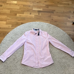 Rutig rosa dam skjorta från Stockh LM - Rosa skjorta från Stockh LM i storlek 36. Skjortan har ett diskret rutigt mönster, klassisk krage och vita knappar framtill. Långärmad modell med broderad logga på bröstet.