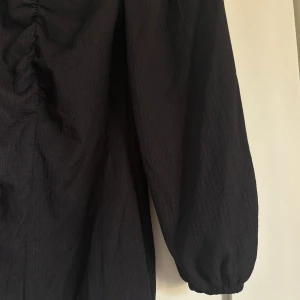 Svart klänning med puffärm från Gina Tricot - Snygg svart klänning från Gina Tricot i storlek XS. Klänningen har puffiga långärmar, en djup fyrkantig ringning och rynkade detaljer framtill. Materialet är lätt strukturerat och ger en cool vibe. Perfekt till alla årstider. Aldrig använd
