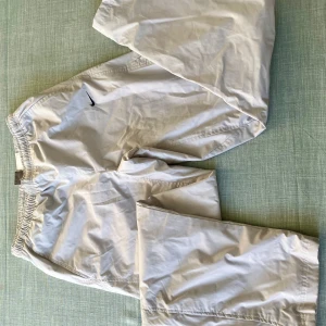 Nike ljusgrå loose pants - Nike fodrade vindbyxor i ljusgrått med elastisk midja och klassisk svart swoosh-logga. Modellen är loose fit och har dragkedja i sidan nedtill. Tillverkade i lätt polyester, fodrade perfekta för kallare dagar.