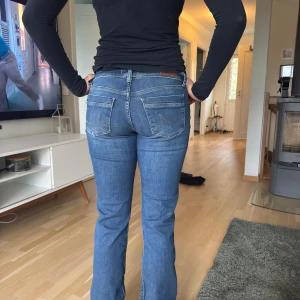 Blå ltb bootcut jeans med låg midja - Snygga blå jeans med bootcut och låg midja. Klassisk femficksmodell med ljus tvätt och diskreta slitningar. Jeansen har raka ben som blir lite vidare nertill och coola detaljer på bakfickorna. Perfekta för en avslappnad och trendig look. hon på bilden är 175