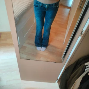 True Religion blå bootcut jeans - Säljer ett par blå jeans från True Religion i klassisk bootcut-modell. Jeansen har snygga kontrastsömmar, ikoniska bakfickor med broderad logga och låg midja. Tillverkade i jeansmaterial med en cool tvättad look. Perfekta för dig som gillar street och retrovibe.