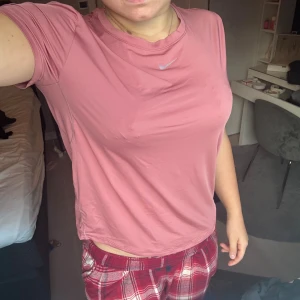Rosa Nike t-shirt i syntetmaterial - Säljer en rosa t-shirt från Nike med klassisk logga på bröstet. T-shirten är kortärmad och har en sportig vibe, perfekt för träning eller chill. Materialet är mjukt och andas, vilket gör den skön att ha på sig hela dagen.