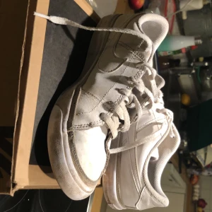 Vita Nike sneakers i skinn - Klassiska vita Nike sneakers i skinn med snörning och rund tå. Snygg och enkel design med diskret Nike-logga på sidan och tungan. Perfekta för en clean och sportig look. Platt sula och bekväm passform. Billigt pris som tyvär inte är förhandlingsbart. Om du har frågor kontakta gärna mig.