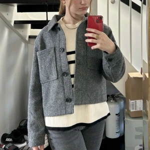 Grå kappa i ull med stora fickor - Säljer en grå overshirt från HM i ullmix med stora bröstfickor och knäppning framtill.
