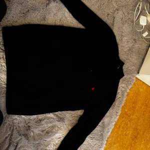 Svart stickad half zip från Giorgio di Mare - Svart stickad tröja från Giorgio di Mare med half zip och hög krage. Tröjan har ett rött broderat segelbåtsmärke på bröstet och ribbade detaljer vid krage och ärmslut. Storlek L, inga defekter! 