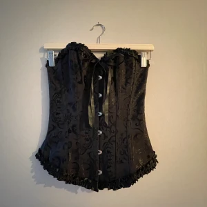 Korsett - Svart korsett med fint mönster och snörning bak. Perfekt till halloween, fest eller temafest.  Använd en gång. 