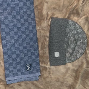 Grå Louis Vuitton damier mössa  - Snygg grå mössa från Louis Vuitton med klassiskt Damier-rutmönster och metallpatch framtill. Tillverkad i 100% ull, designad i Italien. Perfekt för dig som gillar lyxiga accessoarer med streetvibe och vill sticka ut med exklusiv stil. 
