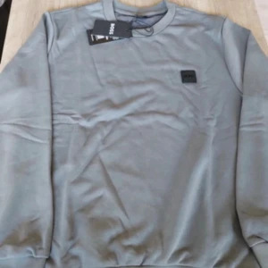 Grå sweatshirt från Hugo Boss - Snygg grå sweatshirt från Hugo Boss med diskret logopatch på bröstet. Tröjan har rund hals, långa ärmar och är tillverkad i mjuk bomull. Perfekt för dig som gillar stilrena och klassiska plagg med en modern touch. OBS PASSAR L-XL