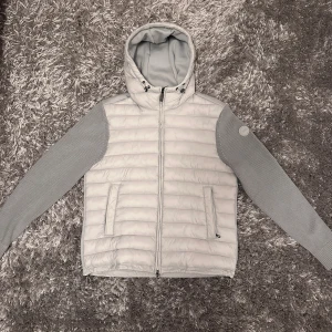 COLMAR grå cardigan jacka - Snygg ljusgrå cardigan från Colmar med stickade ärmar och vadderad kropp. Jackan har huva med snörning, två fickor med dragkedja och Colmar-logga på ärmen. Oanvänd och helt nytt skick.