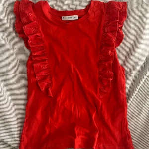 Röd volangtop från MANGO - Snygg röd topp från MNG med volangdetaljer i spets längs axlarna. Modellen är ärmlös och har rund halsringning. Perfekt för dig som vill sticka ut med en färgstark och trendig look.