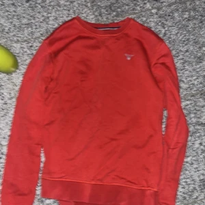 Röd långärmad tröja från GANT - Snygg röd långärmad tröja från GANT med broderad logga på bröstet. Tröjan har en klassisk rund hals och är tillverkad i mjuk bomull som känns skön mot huden. Perfekt för dig som gillar stilrena och enkla plagg med en touch av preppy.