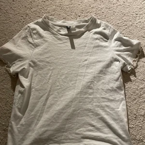 Vit t-shirt med pärldetaljer H&M Divided - Vit t-shirt från H&M Divided i storlek XXS. Klassisk modell med korta ärmar och rund hals. Ärmsluten är dekorerade med pärlor för en extra snygg touch. Tillverkad i mjuk bomull, perfekt för en clean och stilren look.