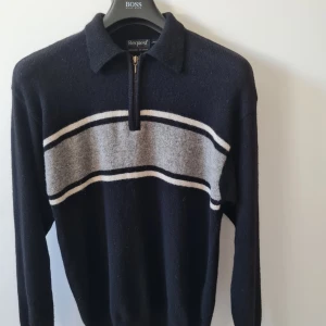 Stickad ulltröja med dragkedja från KappAhl strl S - Säljer en mörkblå stickad tröja från KappAhl med fjärdedels dragkedja och krage. Tröjan har en grå och vit rand över bröstet och långa ärmar. Materialet är en blandning av lammull 80% och polyamid 20%. Storlek S. Kan hämtas i Vallentuna.