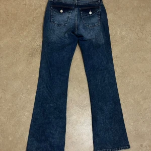 Blå bootcut jeans från Divided - Snygga blå bootcut jeans från Divided med klassisk femficksdesign och markerade bakfickor med lock och knapp. Jeansen har en lätt tvättad look och är tillverkade i jeansmaterial med kontrastsömmar. Perfekta för dig som gillar en avslappnad men trendig stil.