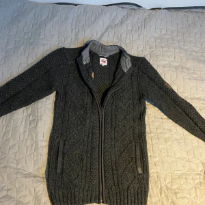 Mörkgrå stickad kofta från Spieth & Wensky - Säljer en mörkgrå stickad kofta från Spieth & Wensky i storlek XS. Koftan har snyggt kabelstickat mönster, hel dragkedja framtill och ribbade muddar. Perfekt för kyliga dagar och har en klassisk, tidlös look.