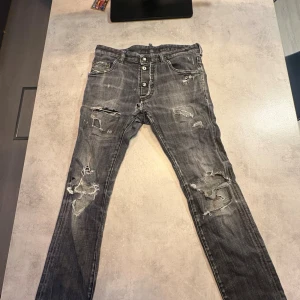 Grå slitna jeans från Dsquared2 - Grå jeans från Dsquared2 med slitna detaljer och trasiga partier på benen. Jeansen har knäppning med tre knappar framtill, klassisk femficksmodell och tydlig Dsquared2-lapp bak i midjan. Modellen är smal och har en cool, streetig vibe.