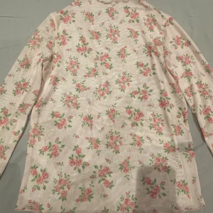 Blommig långärmad mesh tröja - Säljer en söt långärmad mesh tröja med blommigt mönster i rosa och grönt på en ljus bakgrund. Perfekt för dig som gillar romantiska och mjuka vibes. Tröjan har en hög krage och är gjord i ett tunt, mjukt material som känns skönt mot huden.