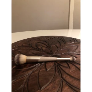 Flaer - Duo sminkborste i beige och guld - Snygg Flaer - duo sminkborste med två olika borstar, i ena änden en större fluffig borste och i andra änden en mindre rundad borste. Handtaget är beige med guldiga detaljer och borstarna är gjorda av mjuka syntetiska strån. Perfekt för både bas och detaljer.