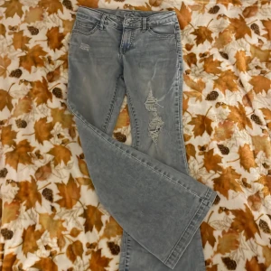 Bootcut jeans från Art Class, ljusblå - Bootcut jeans i ljusblå tvätt från Art Class med slitna detaljer och hål på ena benet. Klassisk femficksmodell, bälteshällor och dragkedja. Snyggt avslappnad look med bredare ben och coola slitningar.