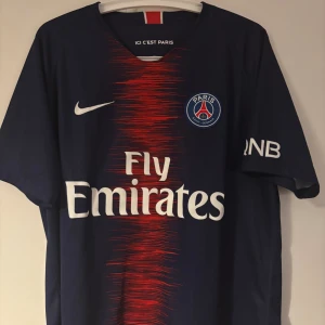 PSG matchtröja Nike Dri-Fit (storlek L) - Snygg Paris Saint-Germain tröja i originaldesign från Nike med “Fly Emirates”-sponsor. Mörkblå med röd mittdetalj och PSG-logga på bröstet. Bekväm Dri-Fit-modell i storlek L – perfekt för både träning och vardag. I mycket bra skick, knappt använd.