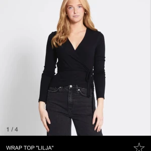 Svart omlottopp Lilja med knyt - Svart omlottopp från Lager157 med långa ärmar och v-ringad hals. Toppen har ett knyt i midjan som ger en figurnära passform. Materialet är mjukt och stretchigt. Toppen är helt oanvänd i storlek XS.
